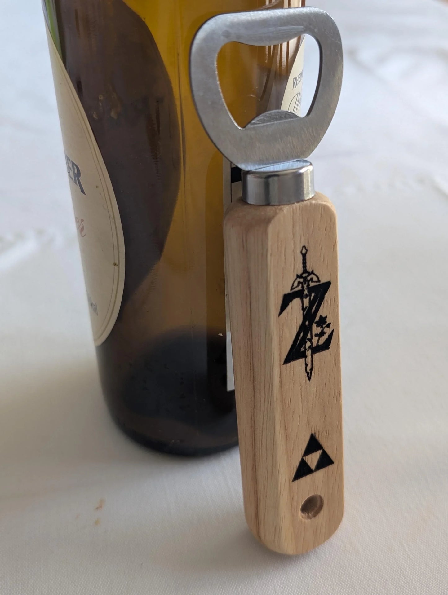 Wooden bottle opener with engraved sword and triangle design beside a wine bottle